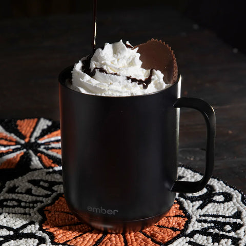 A Black Ember Mug² is filled with whipped cream and topped with a peanut butter cup.